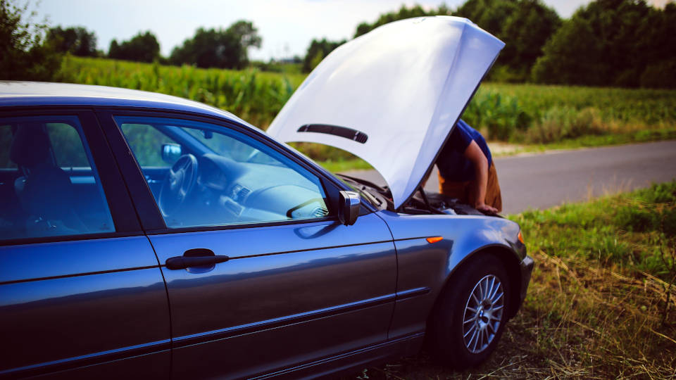 A picture of a broken down car with the hood up and a man looking under the hood.