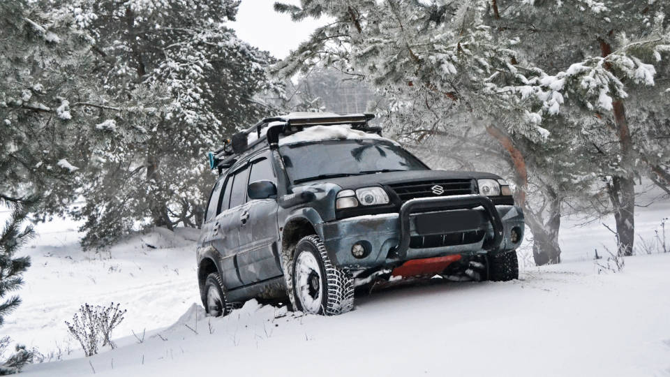 A picture of a Suzuki all-wheel-drive off-roading in deep snow in the forest.