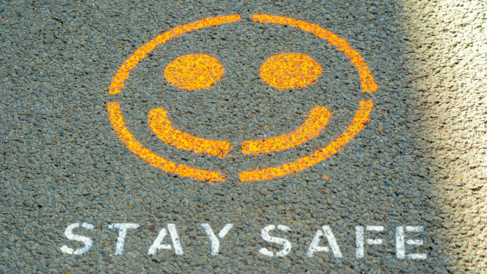 A picture of a yellow happy face spray-painted on the asphalt with the words Stay Safe printed underneath.