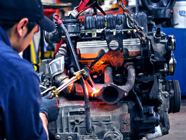 Mechanic welding exhaust manifold on engine.
