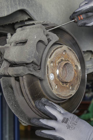 A picture of a mechanic inspecting disc brakes; the brake rotors, brake pads, and brake calipers.