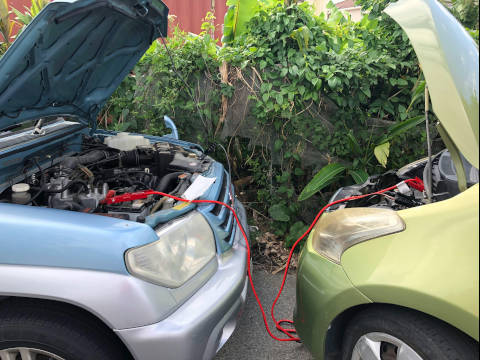 A picture of two cars facing front to front with booster cables attached for jump starting the car.